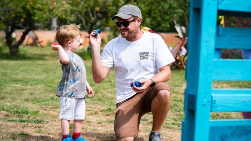 A father and son smile at each other while trying out the beanbag toss at Summer of Play